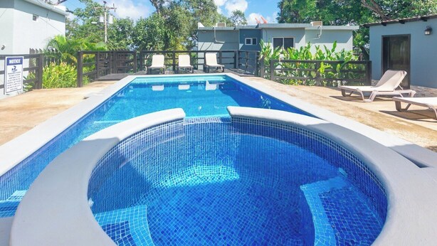 Ein rechteckiger Pool mit Fliesenbord, umgeben von Liegestühlen und einem Holzzaun.