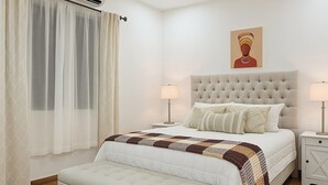 Ein Schlafzimmer mit Bett, Nachttischen, Vorhängen an einem Fenster und einem Deckenventilator.