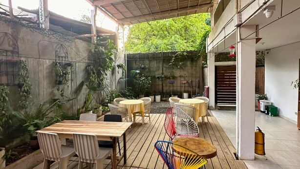 An outdoor patio with wooden tables and chairs, surrounded by potted plants and a concrete wall. - Casa Colibri Palomino (Palomino)