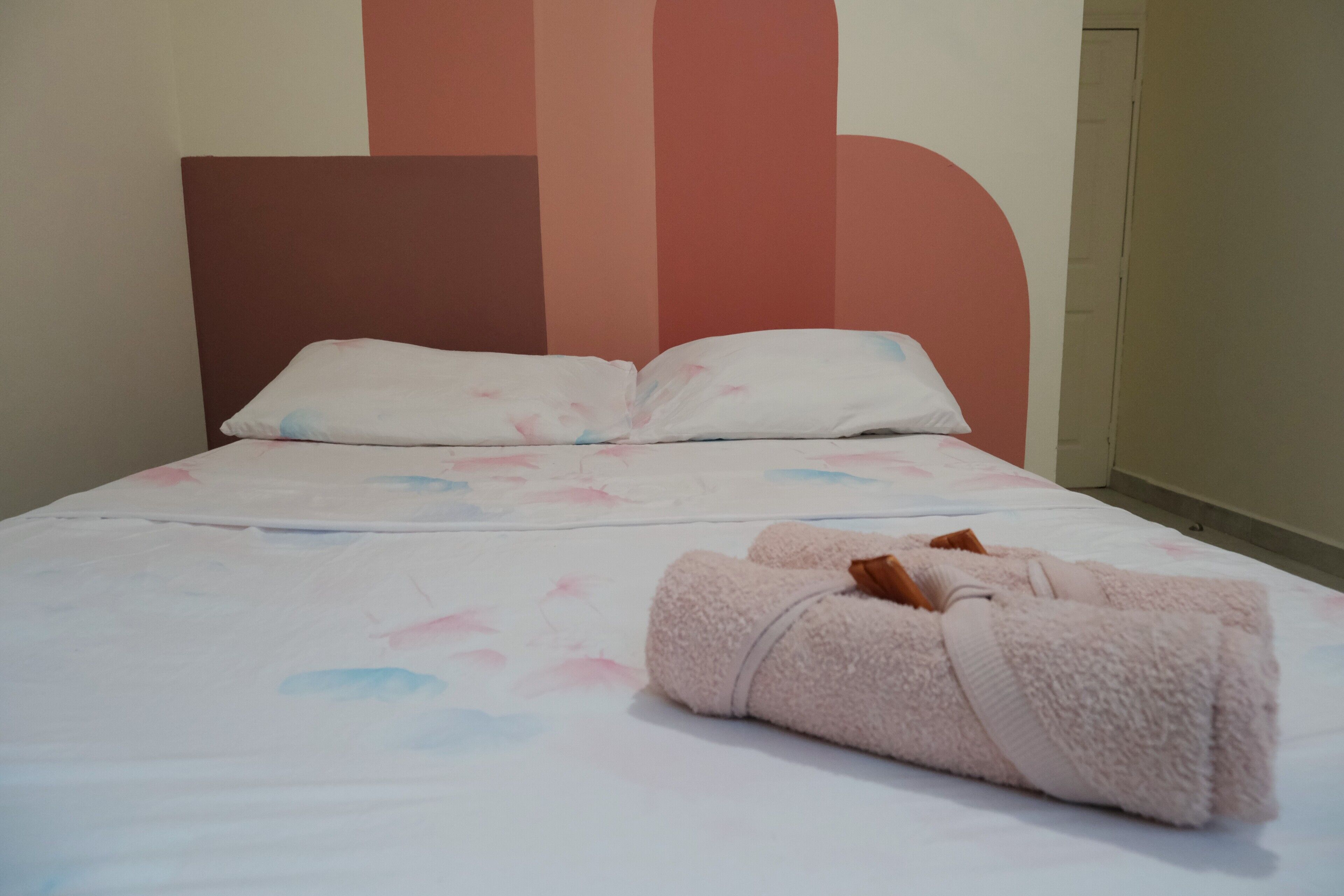 A neatly made bed with a floral-patterned bedspread and two pillows. A rolled-up towel is placed on the bed.