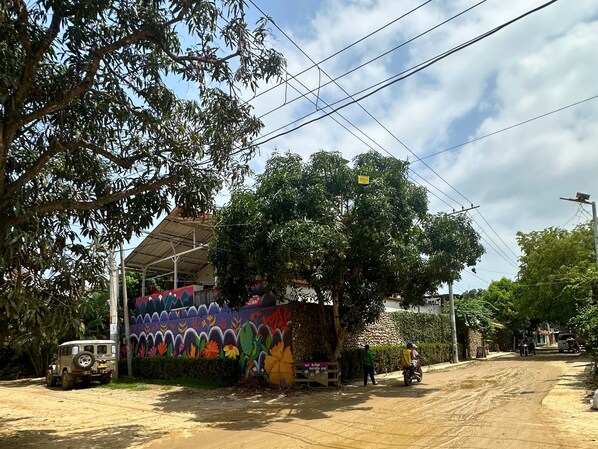A dirt road with a mural on a building, a jeep, and a motorcycle.