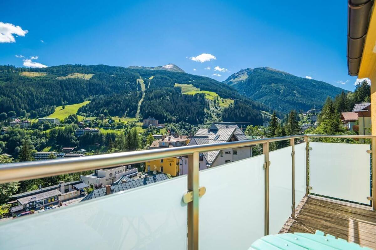 Un balcon offrant une vue sur un paysage montagneux, une ville en contrebas et un ciel bleu dégagé.
