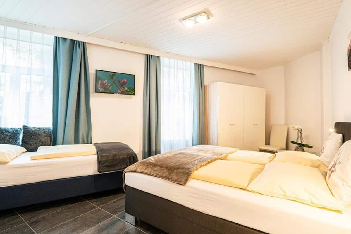 Une chambre d’hôtel avec deux lits, une armoire, un bureau et une fenêtre avec des rideaux.