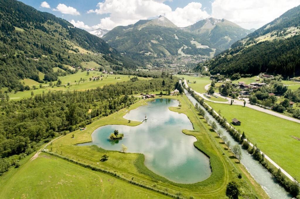 A mountainous landscape with a river running through a valley, surrounded by green fields and small buildings.