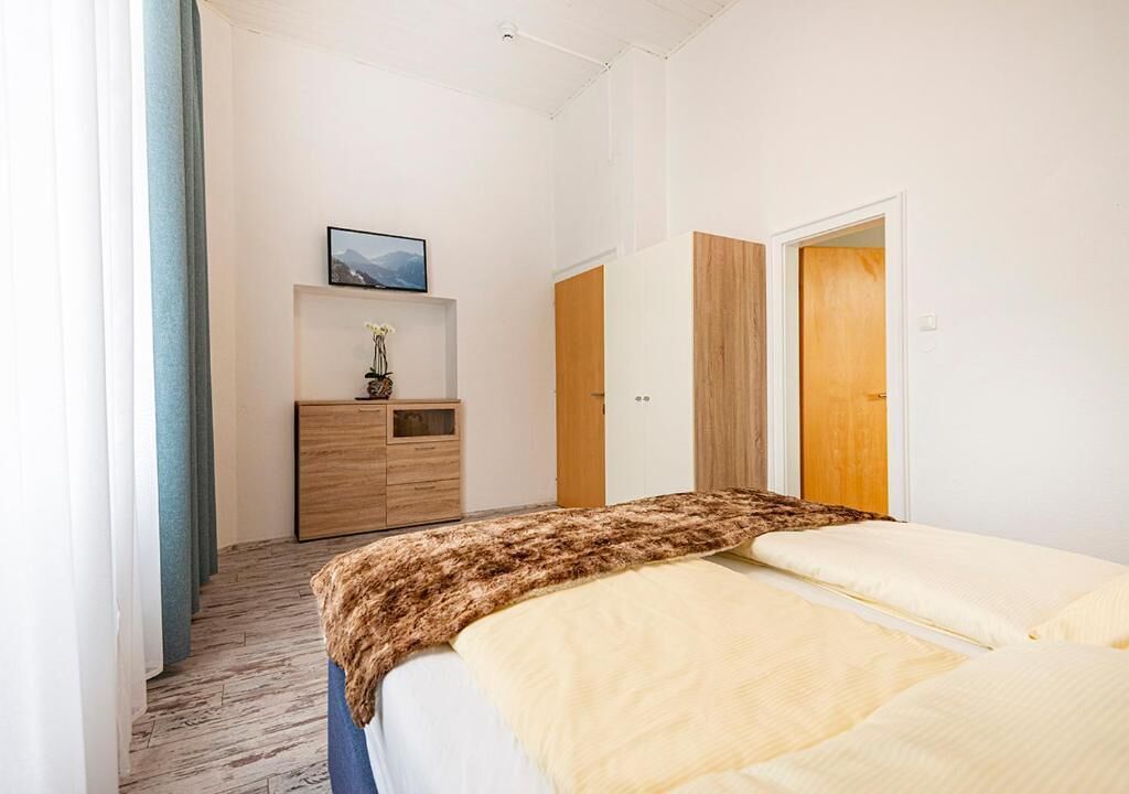Een slaapkamer met een bed, een ladekast, een spiegel en een deur.