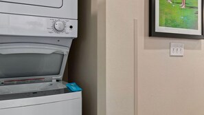Eine Waschmaschine mit Frontlader, einem blauen Waschmittelbeutel und einem gerahmten Bild an der Wand.