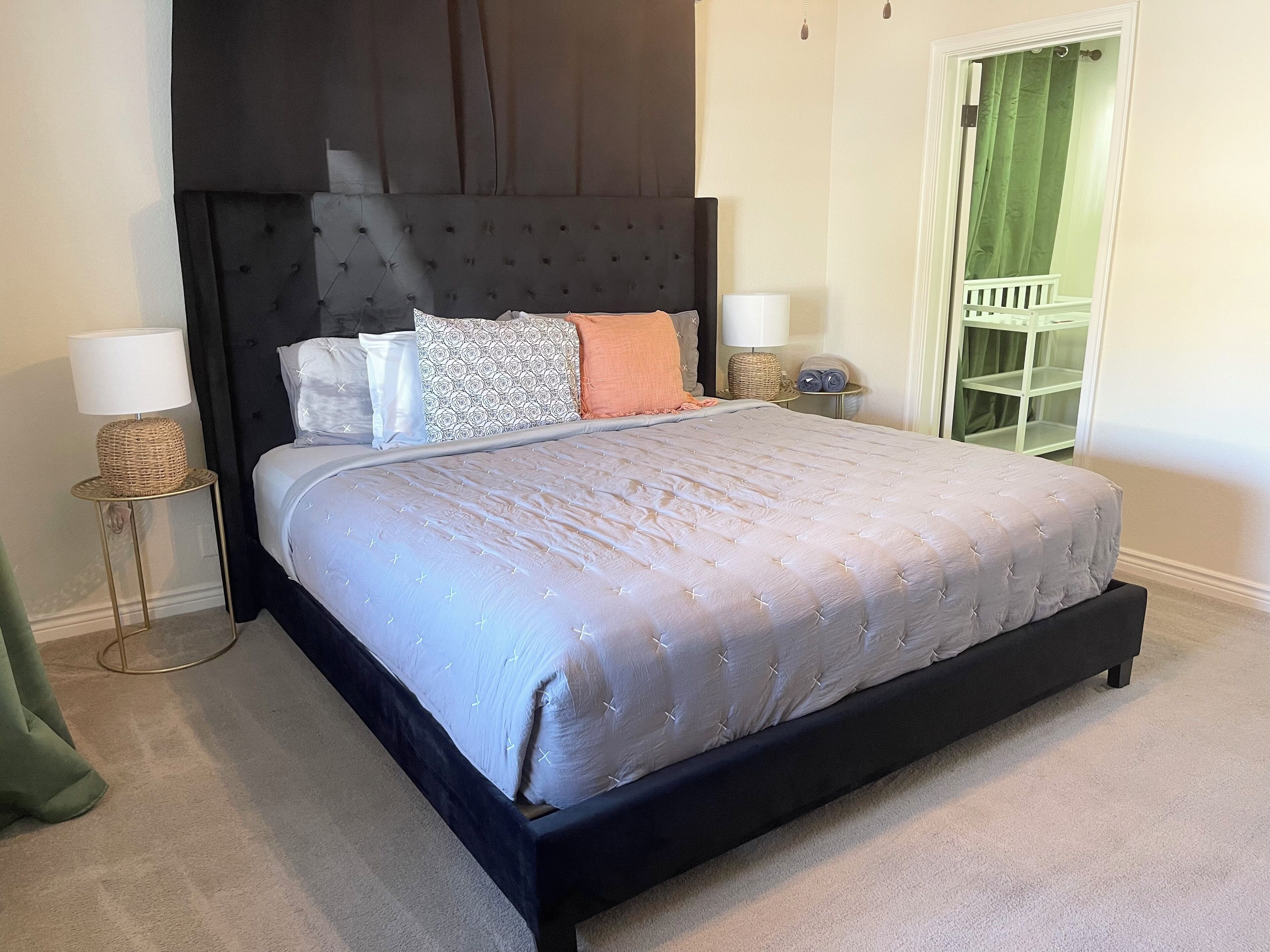 A bedroom with a large bed, dark headboard, two bedside tables with lamps, a green curtain, and a white door.
