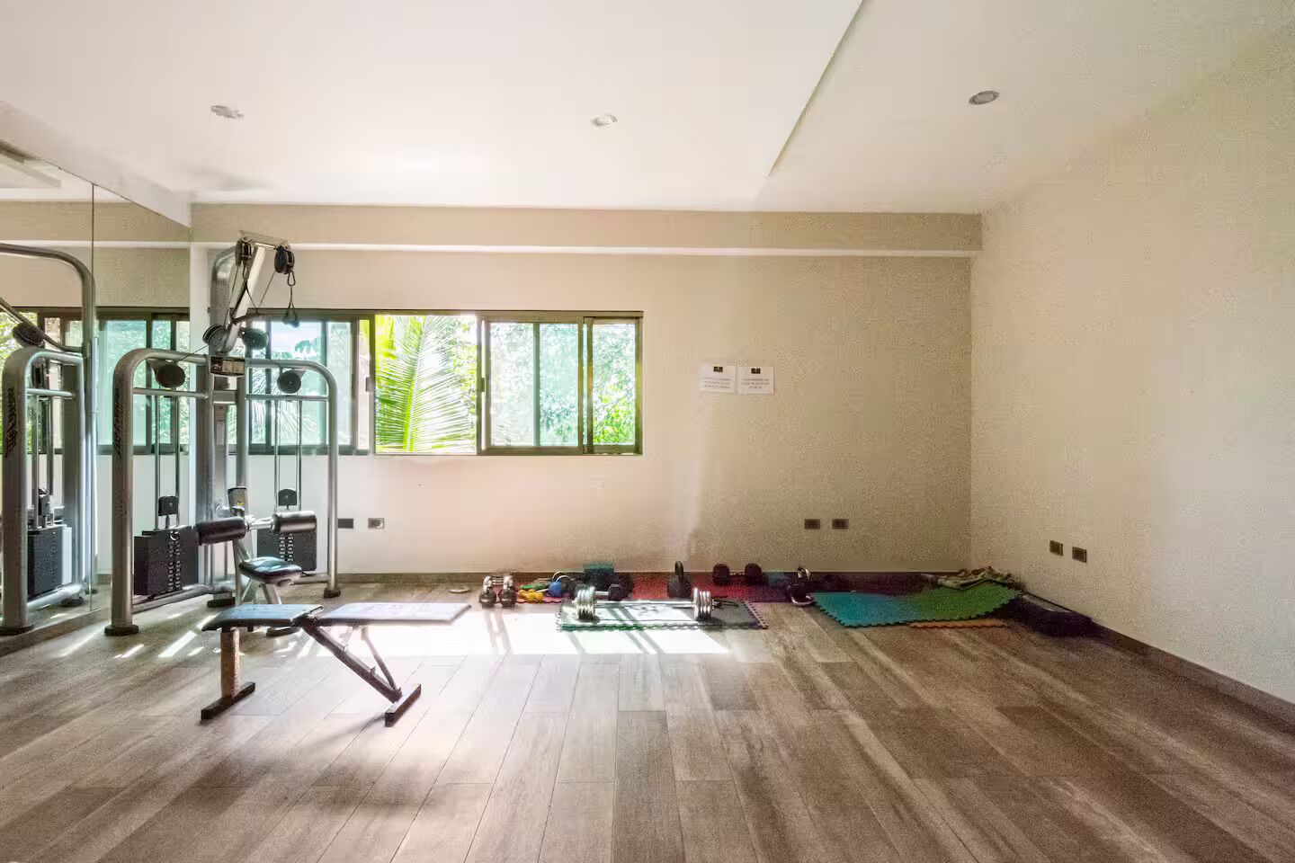 A spacious room with a large window, a gym with various exercise equipment, and a yoga mat on the floor.