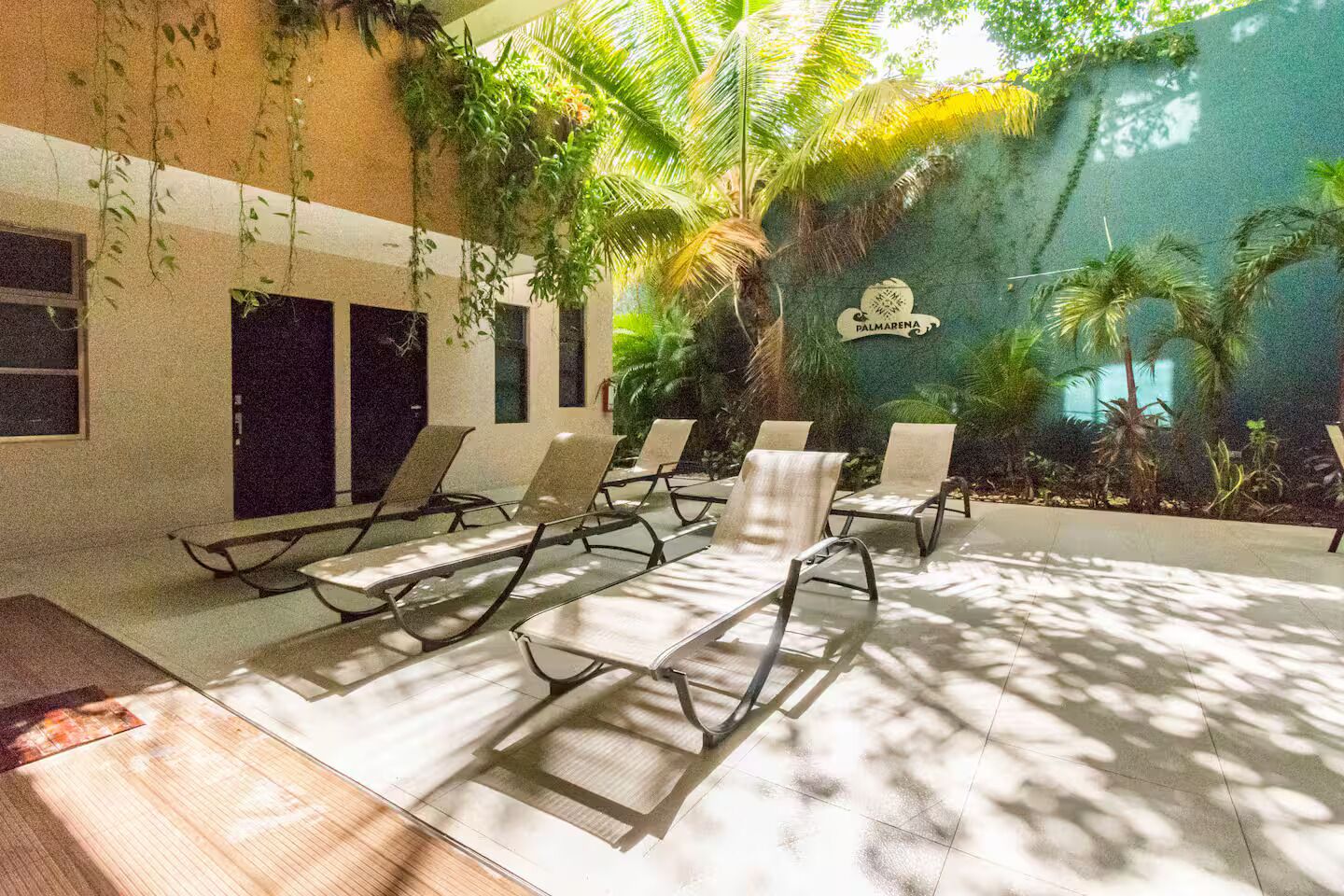 Un espace piscine aménagé avec des chaises longues, des palmiers et un panneau indiquant « Palmarena ».