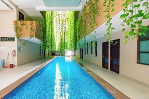 Une piscine intérieure à l’eau d’un bleu limpide, entourée de murs ornés de lianes vertes retombantes.