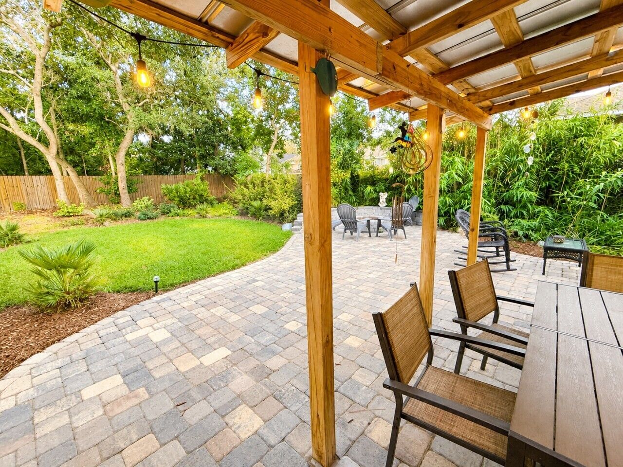 An outdoor patio with wooden pergola, stone flooring, and outdoor furniture.
