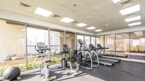 A gym with exercise equipment, large windows, and a view of buildings outside. - Vogue | Jeewar By Badr JVC near Circle Mall (Dubai)