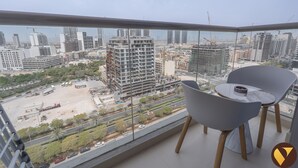 A balcony with a view of a cityscape, including high-rise buildings and construction sites. There are two grey chairs and a small table with a cup on it. - Vogue | Jeewar By Badr JVC near Circle Mall (Dubai)