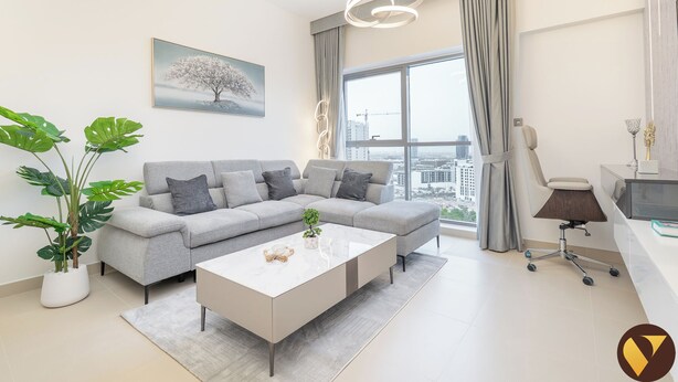 A modern living room with a grey sofa, a white coffee table, and a large window with a view of the city. - Vogue | Jeewar By Badr JVC near Circle Mall (Dubai)