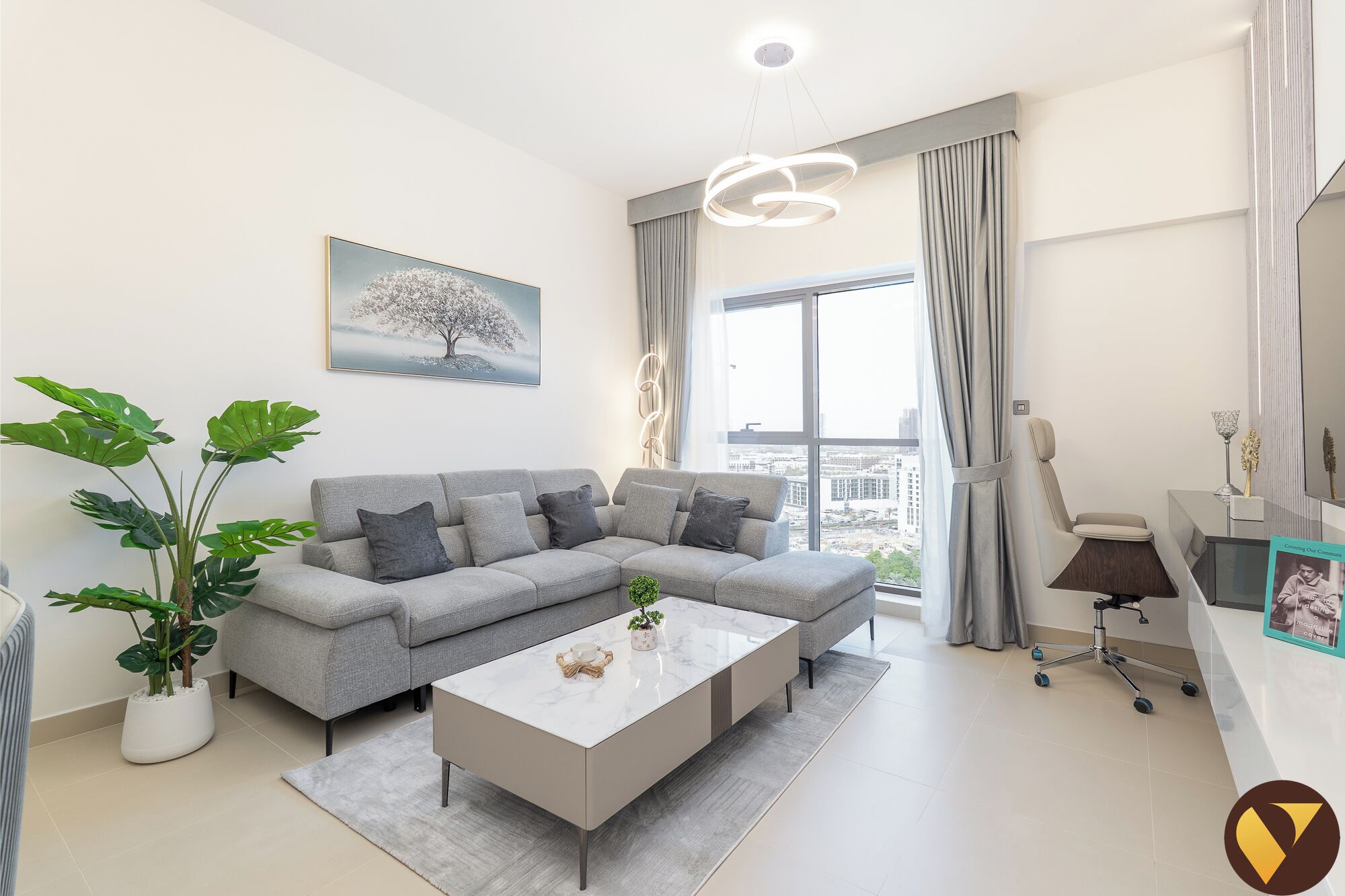 Ein modernes Wohnzimmer mit grauem Sofa, weißem Couchtisch und großem Fenster mit Vorhängen.