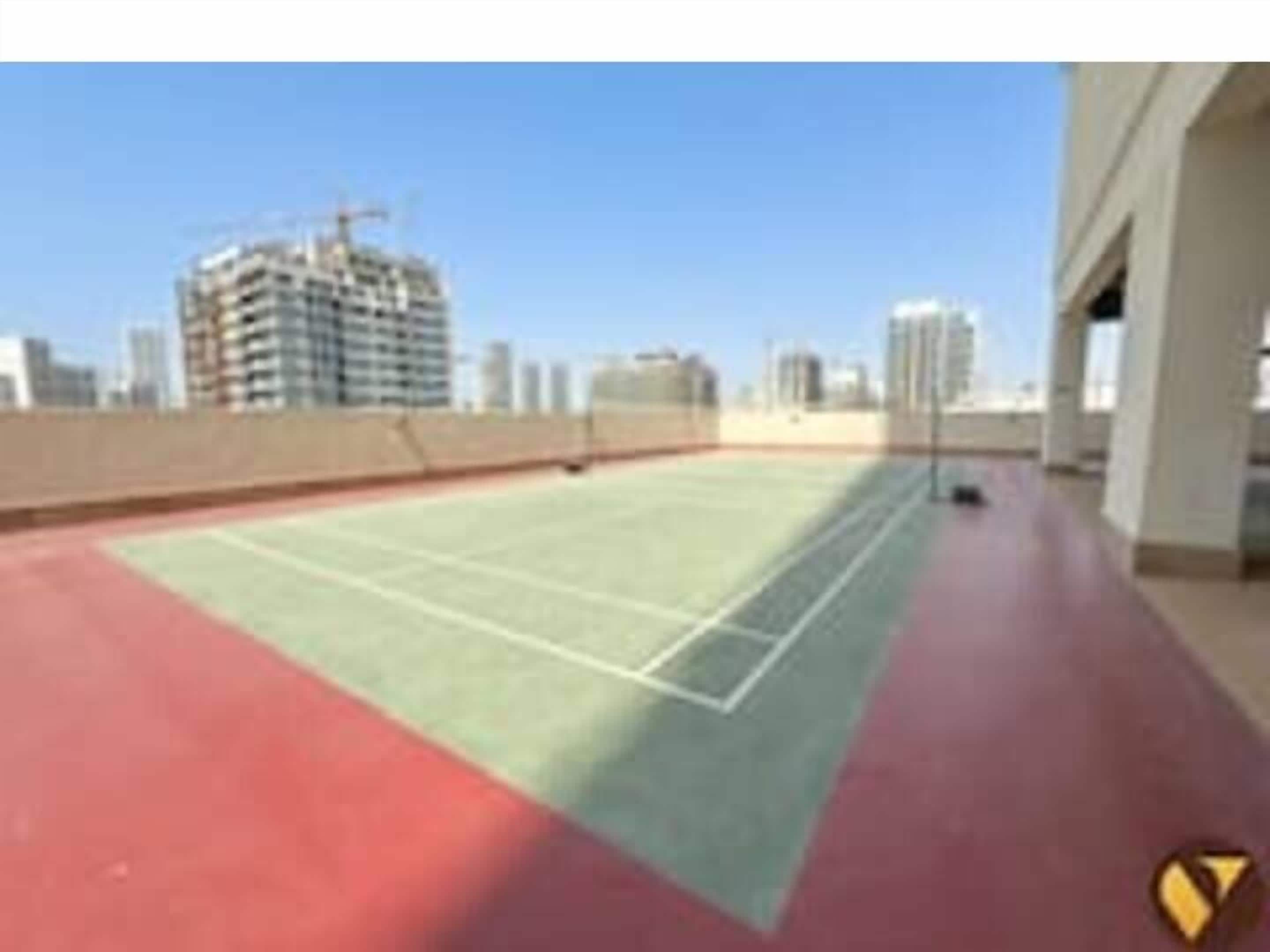 A rooftop tennis court with a red and green surface, surrounded by high-rise buildings.
