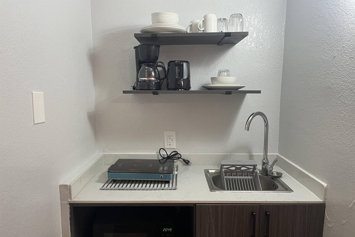 Eine kleine Küche mit Mikrowelle, Kaffeemaschine, Toaster, Spüle und einem Regal mit Geschirr und Gläsern.