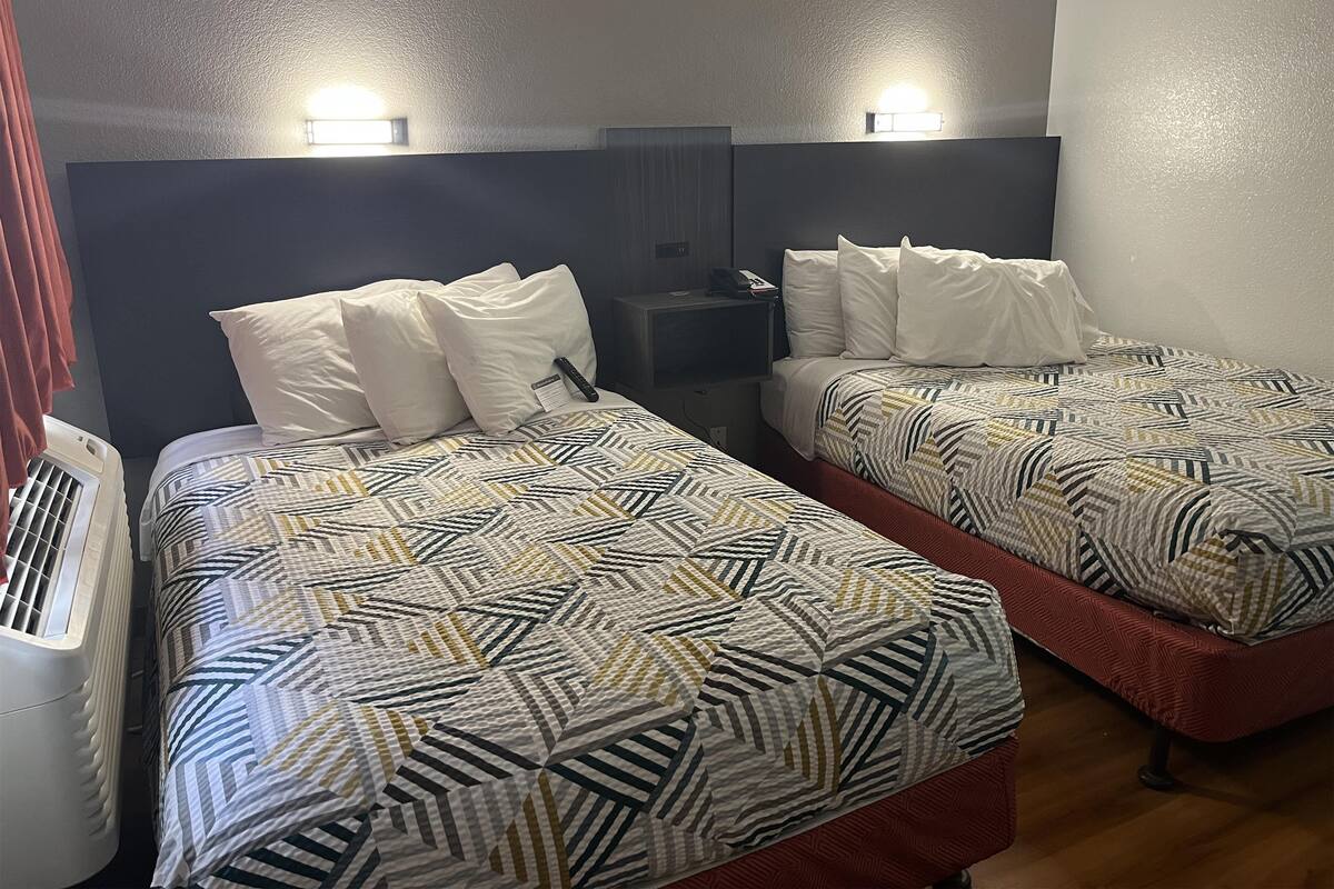 Ein Hotelzimmer mit zwei Betten, jeweils mit gemusterten Bettbezügen und weißen Kissen. Über den Betten befinden sich Wandleuchten und an jedem Bett steht ein kleiner Nachttisch mit einem Telefon.