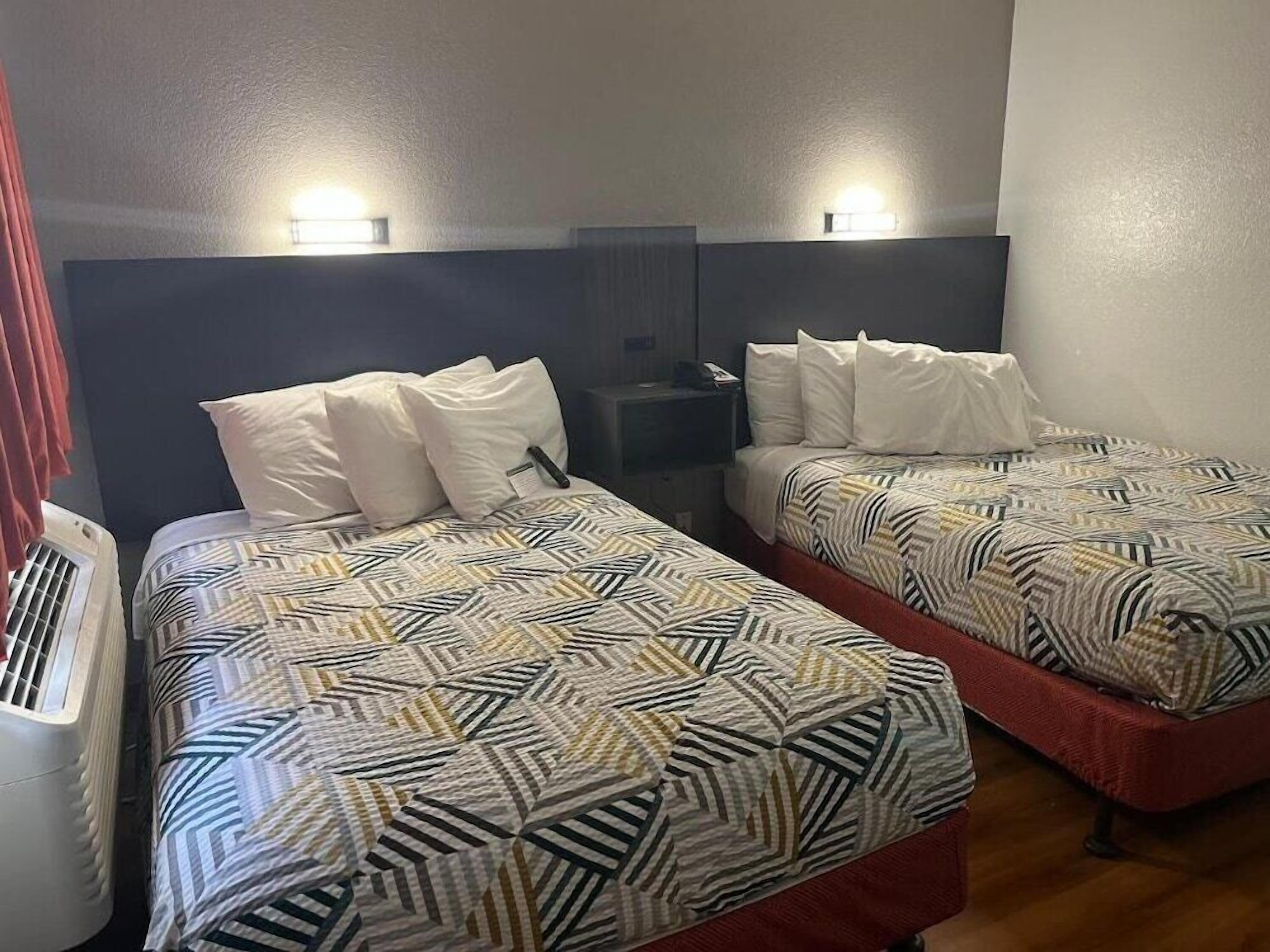 Ett hotellrum med två sängar, båda med mönstrat sänglinne och vita kuddar. Det finns sängbord med lampor och ett litet skrivbord med en telefon.