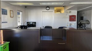 A reception area with a desk, computer, and a security camera. There is a door with a notice sign and a fire alarm. - Studio 6 – Grants, Nm (Grants)