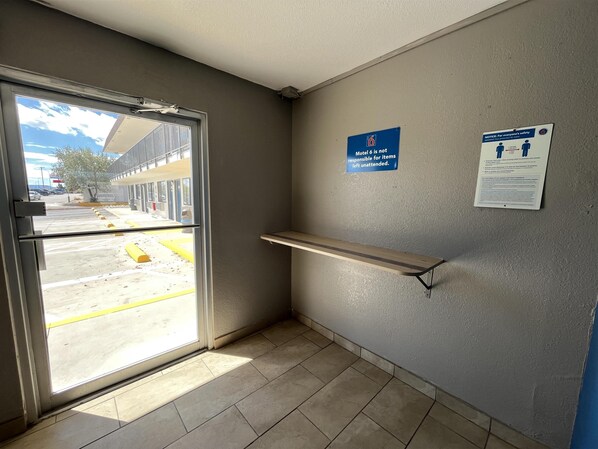 A motel interior with a door leading outside, a wall-mounted shelf, and two safety notices. - Studio 6 – Grants, Nm (Grants)