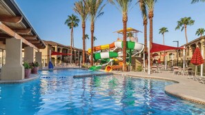 Una piscina con uno scivolo acquatico, palme e lettini.