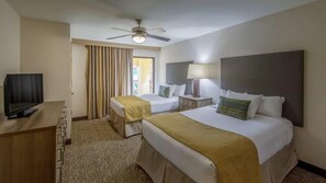 Una camera d'albergo con due letti, una televisione, un ventilatore a soffitto e una finestra con tende.
