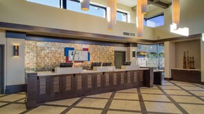 Un'area della reception di un hotel con parete in pietra, un banco accettazione e vista sull'esterno.