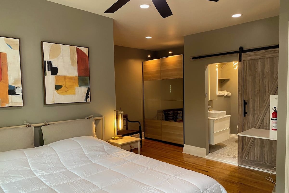 A modern bedroom with a large bed, a bedside table, a chair, and a walk-in closet with a mirror and shelves.