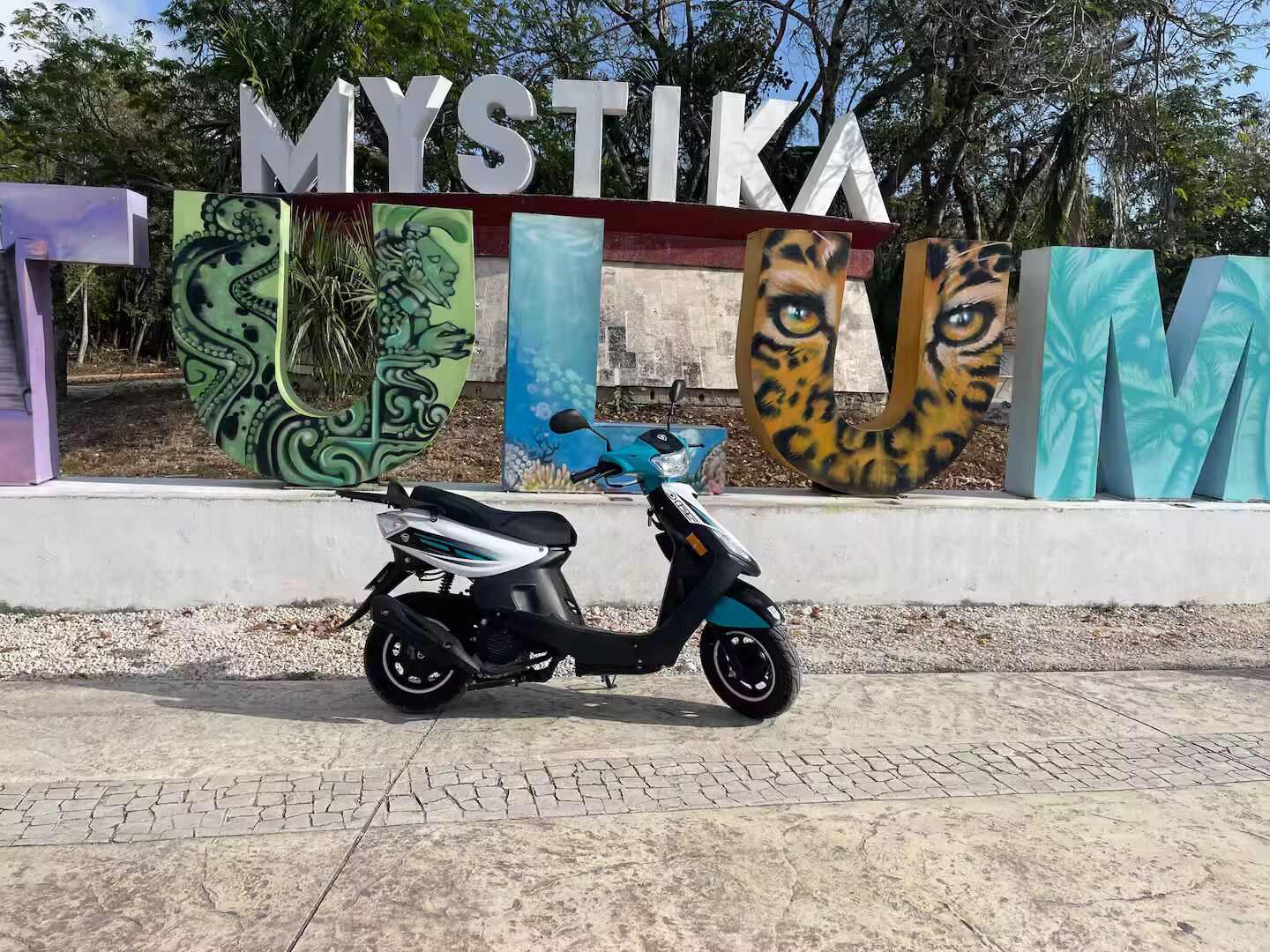 A scooter parked in front of a sign with stylized animal faces and the word "MYSTIKA" on a building.