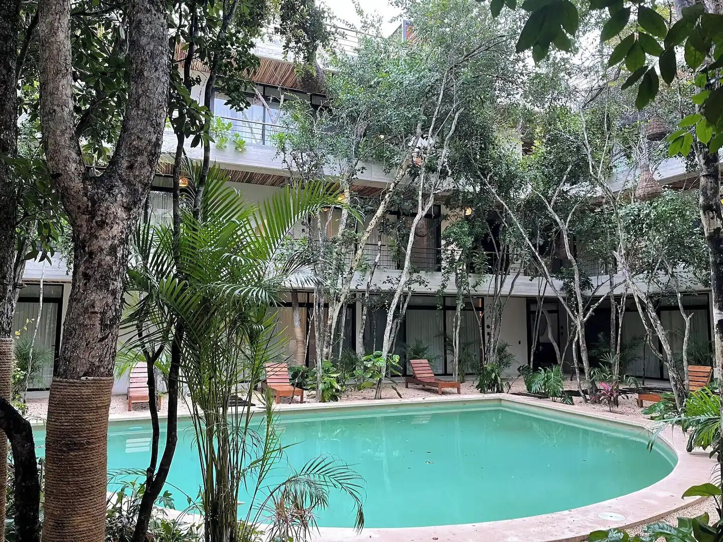 Une piscine entourée d’arbres et un bâtiment doté de nombreux balcons.