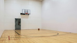 A basketball court with a hoop, wooden floor, and white walls.