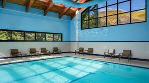 An indoor swimming pool with clear blue water, wooden ceiling beams, and a view of autumn foliage through large windows. - Mountain Getaway: Studio with Kitchen & Fireplace at Vail (Vail)