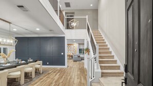 A spacious living area with a wooden floor, a dining table with chairs, a staircase, and a modern chandelier.