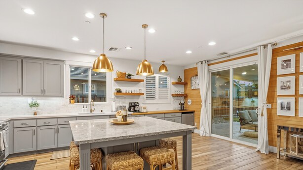 A modern kitchen with a central island, pendant lights, and wooden flooring.
