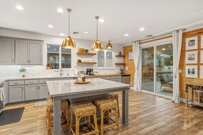 A modern kitchen with a central island, pendant lights, and wooden flooring. - NEW Stylish 5-Bed, 3-Bath Home Near Downtown with EV Charger (West Sacramento)