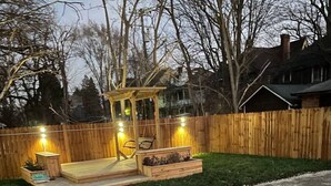 Un patio trasero con terraza de madera, un sendero de piedra y una valla de madera.