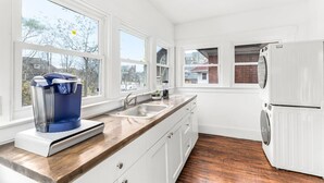 Una cocina moderna con armarios blancos, encimera de madera, cafetera integrada, fregadero y refrigerador.