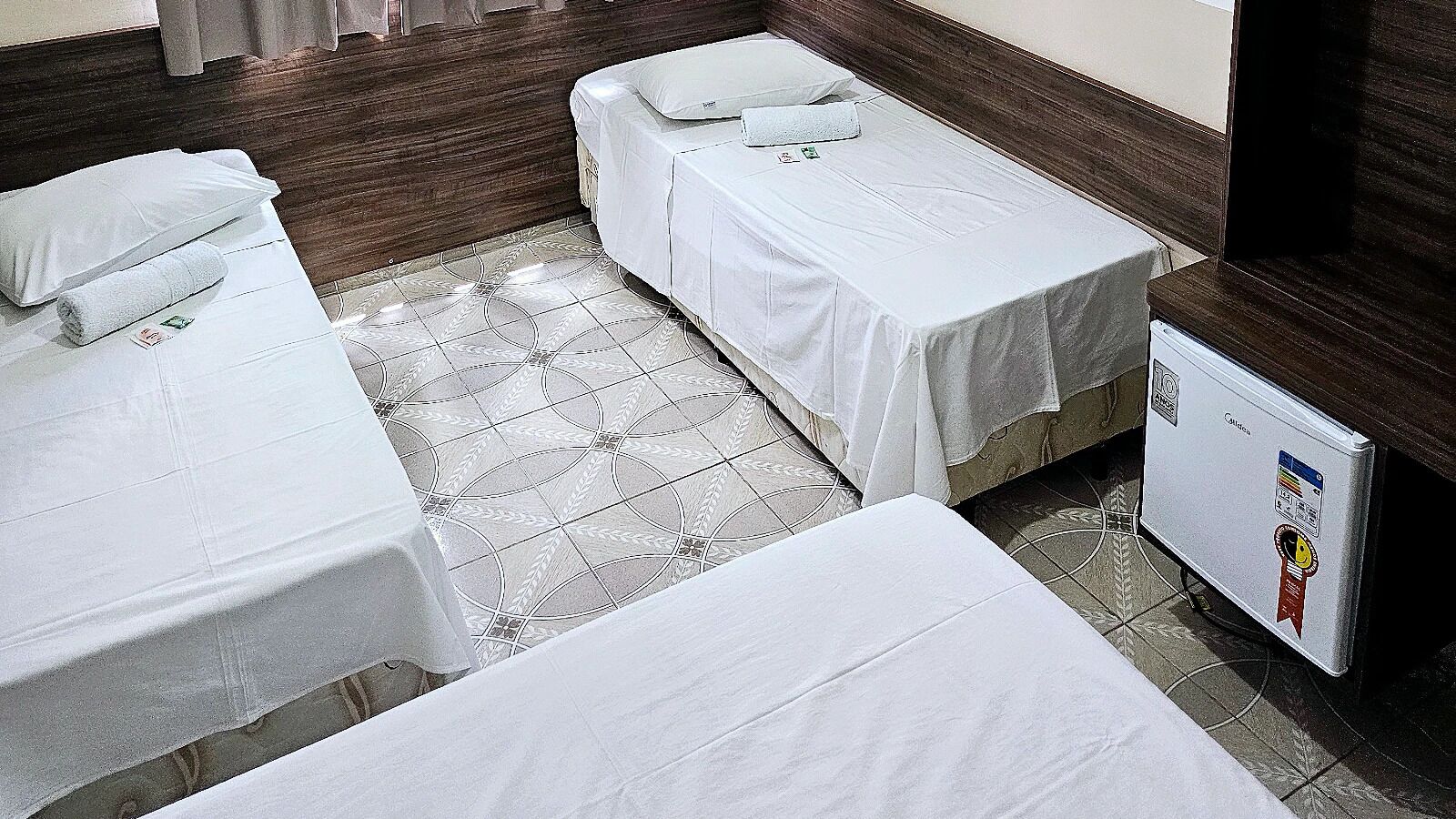 Habitación de hotel con dos camas individuales, un refrigerador pequeño y piso de baldosas.