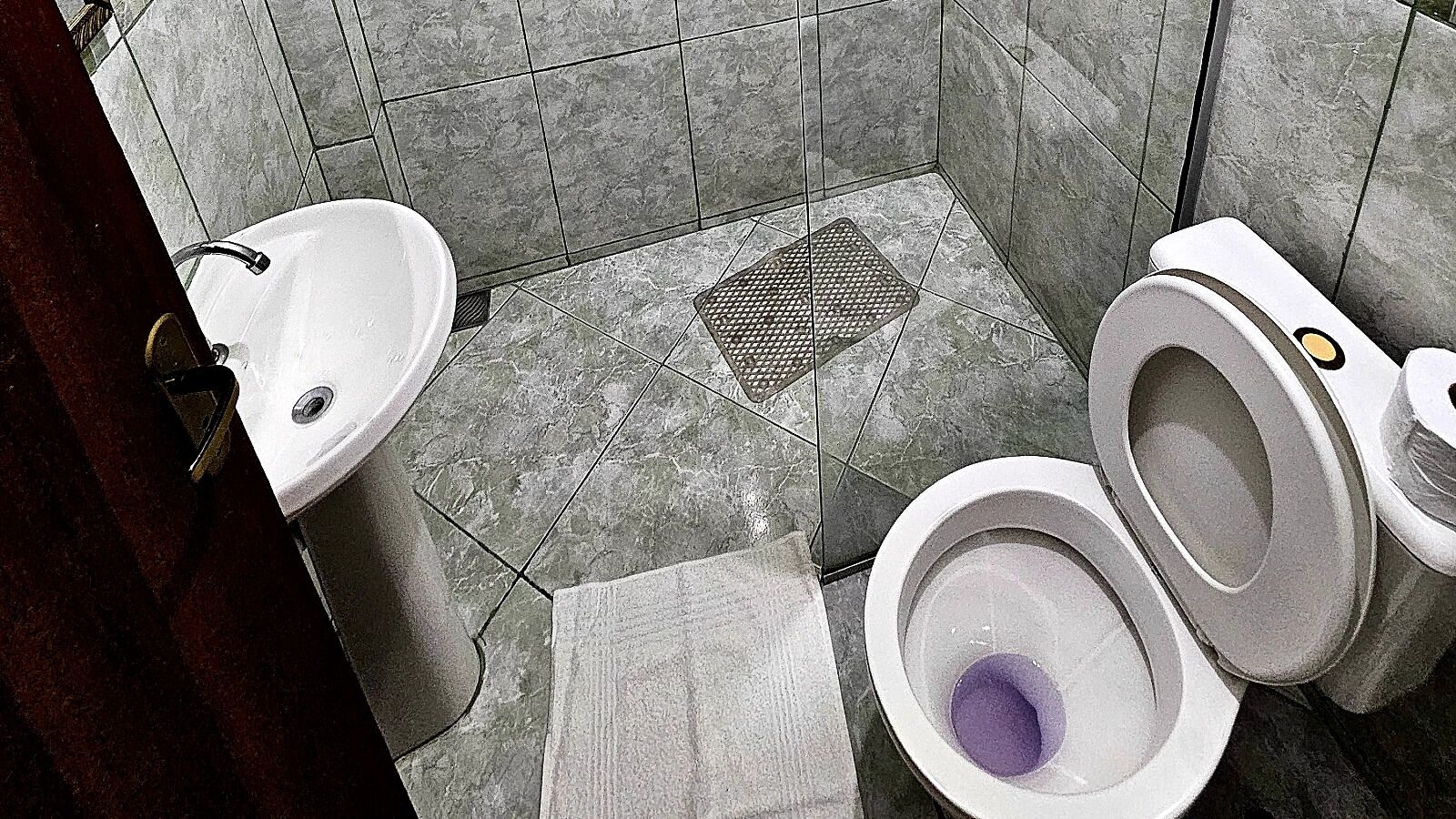 A bathroom with a toilet, sink, and a drain grate on the floor.