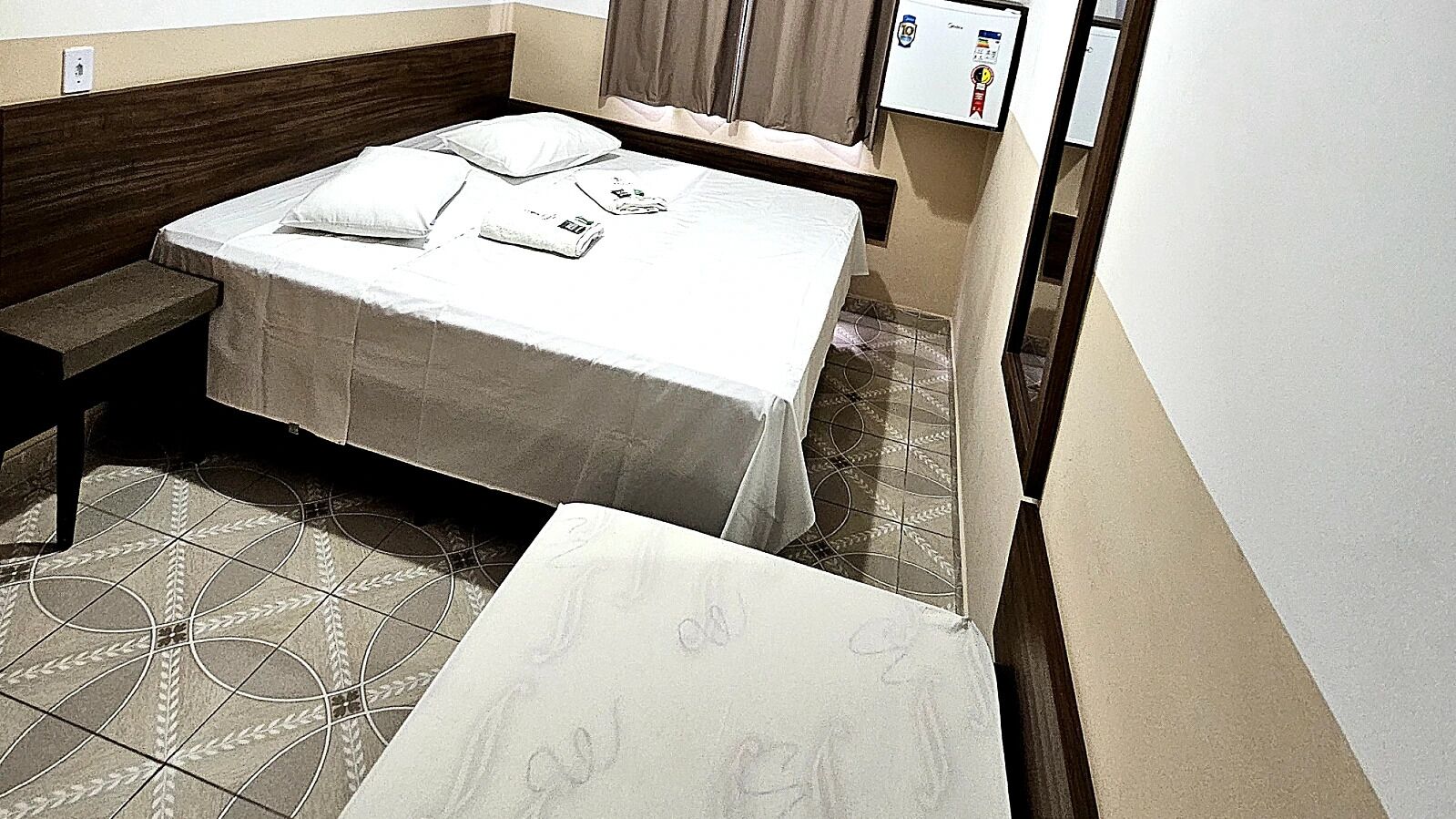A hotel room with a bed, a bench, and a small table.
