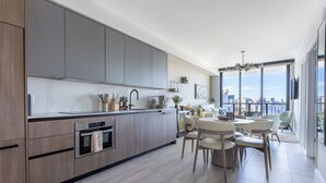 Een moderne keuken met grijze kastjes, een ingebouwde oven en een eethoek met een ronde tafel en stoelen.