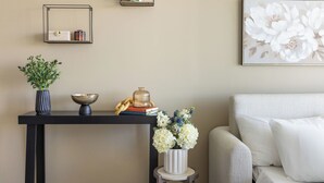 Een woonkamer met een zwarte console tafel, een witte bank en een wandplank met een plant en decoratieve objecten.