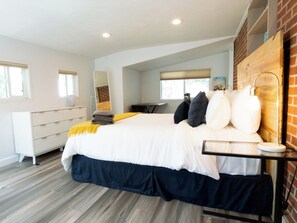 A modern bedroom with a large bed, a desk, and a brick wall. - Your Boulder Home Base, Walk to Pearl St, 2BR/2BA + Parking! (Boulder)