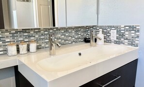A bathroom with a white sink, two faucets, and a mirror above. There are three jars with lids on the countertop. - Your Boulder Home Base, Walk to Pearl St, 2BR/2BA + Parking! (Boulder)