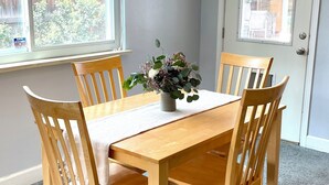 Ein Esszimmer mit Holztisch, vier Stühlen, einem Deckenventilator und einem Fenster mit Blick auf einen Holzzaun und Grünpflanzen.