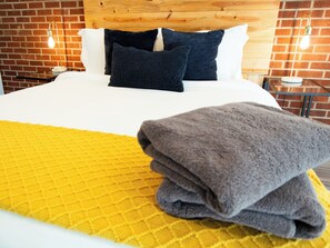 Una cama con cabecera de madera, dos almohadas, un edredón amarillo y una toalla gris doblada.