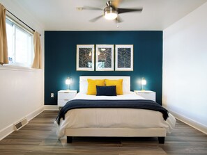 A bedroom with a bed, two bedside tables, a ceiling fan, and artwork on the wall.