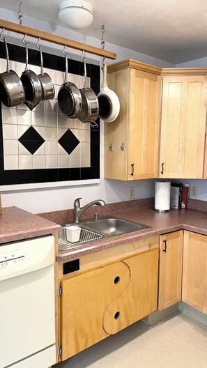 A kitchen with wooden cabinets, a stainless steel sink, and a dish rack with pots and pans.
