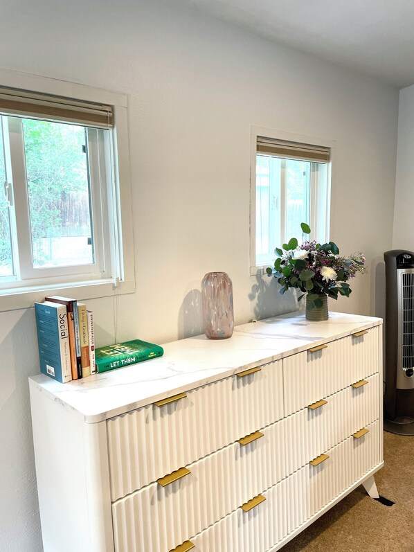 A white dresser with gold handles, a vase with flowers, and books on top.